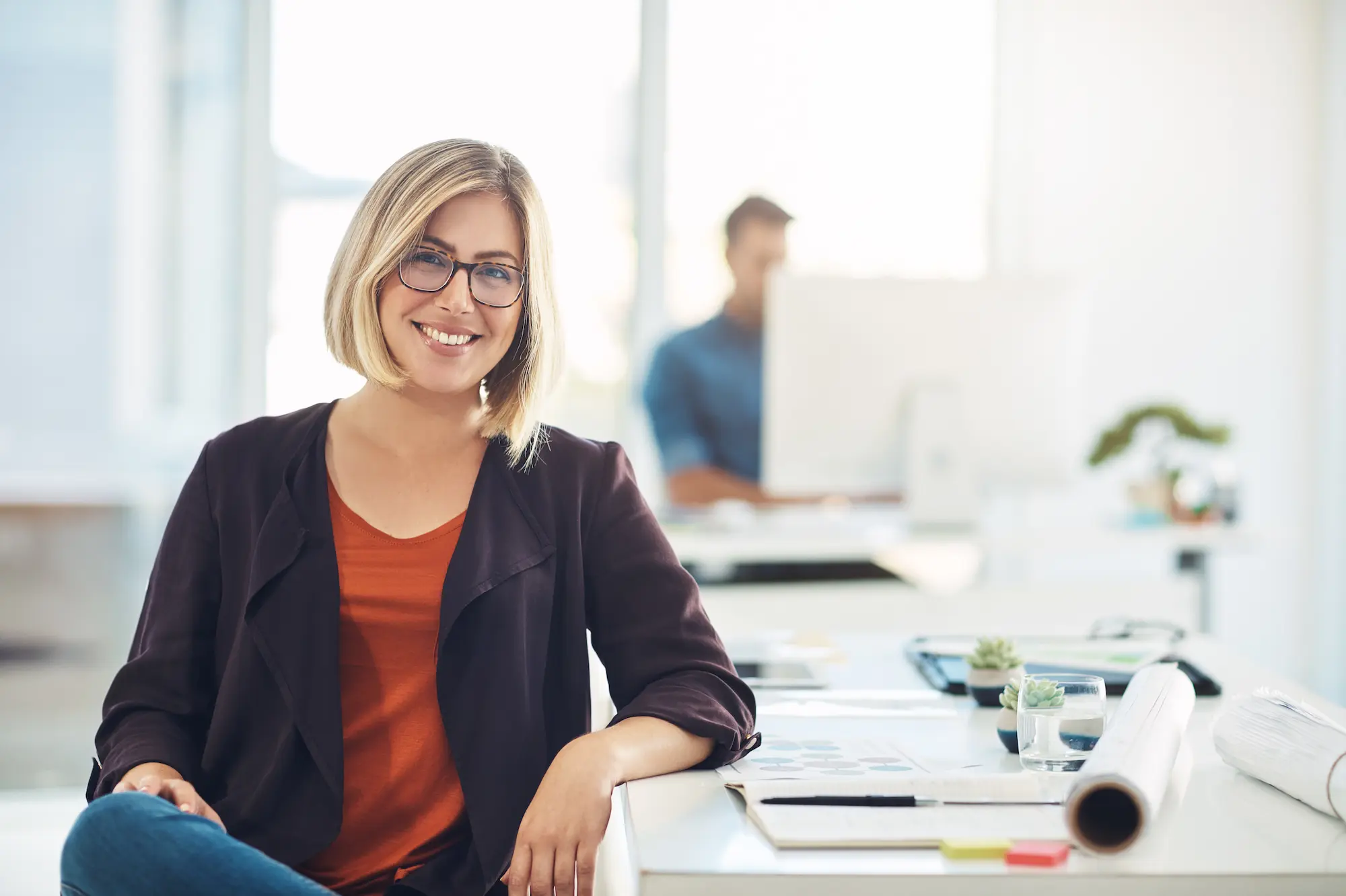 Woman sitting in brightly lit office smiling at camera.